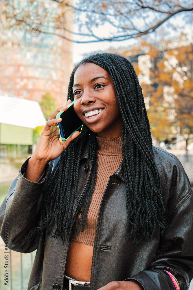 Vertical individual portrait of a happy african american woman smiling and talking by cellphone outdoors. Young female chatting on a call conversation by smartphone. Communication concept. High Vertical individual portrait of a happy african american woman smiling and talking by cellphone outdoors. Young female chatting on a call conversation by smartphone. Communication concept. High