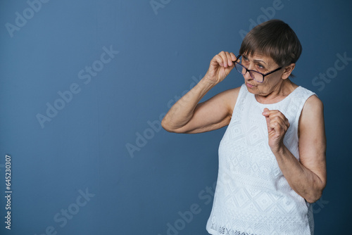 Portrait of an elderly woman on a gray-blue background attentively looking at something through glasses