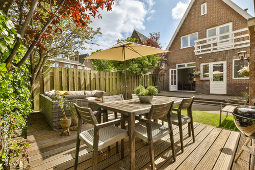 Photography a patio with chairs and an umbrella over the table in front of a large brick hou