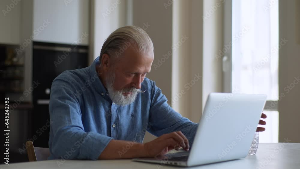 Senior aged bearded man talks via laptop at home. Communication, online meeting and businessman working on computer in living room with fresh water. Useful habits and healthy lifestyle, drinks water. Senior aged bearded man talks via laptop at home. Communication, online meeting and businessman working on computer in living room with fresh water. Useful habits and healthy lifestyle, drinks water.
