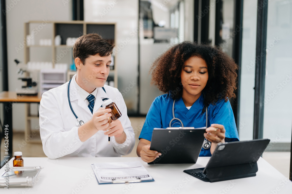 Focused mature male doctor and African female nurse look at tablet and laptop discuss anamnesis together. Concentrated diverse medical professionals in hospital. Focused mature male doctor and African female nurse look at tablet and laptop discuss anamnesis together. Concentrated diverse medical professionals in hospital.