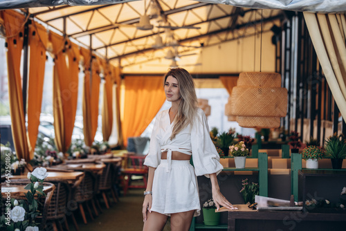 Beautiful blonde model woman, fashionable in a white suit, posing in a summer cafe