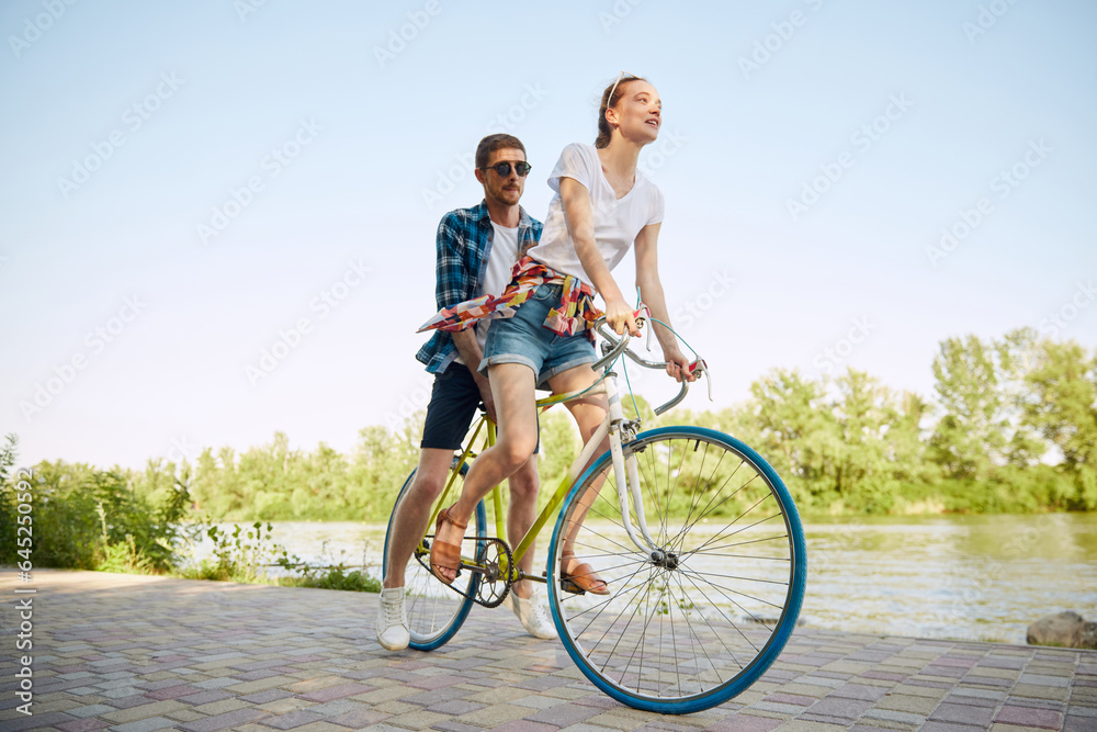 Portrait of young couple, woman and her boyfriend going for a bike ride in river enbankment on summer day. Romantic date concept.