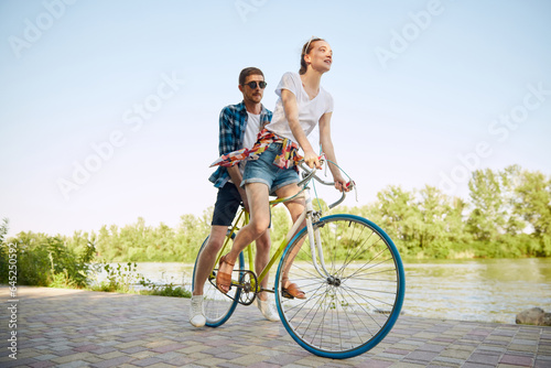 Portrait of young couple, woman and her boyfriend going for a bike ride in river enbankment on summer day. Romantic date concept.