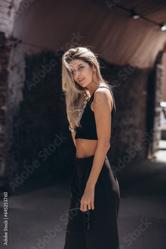 Beautiful blonde model woman  fashionable in a black suit  poses against the walls of a building