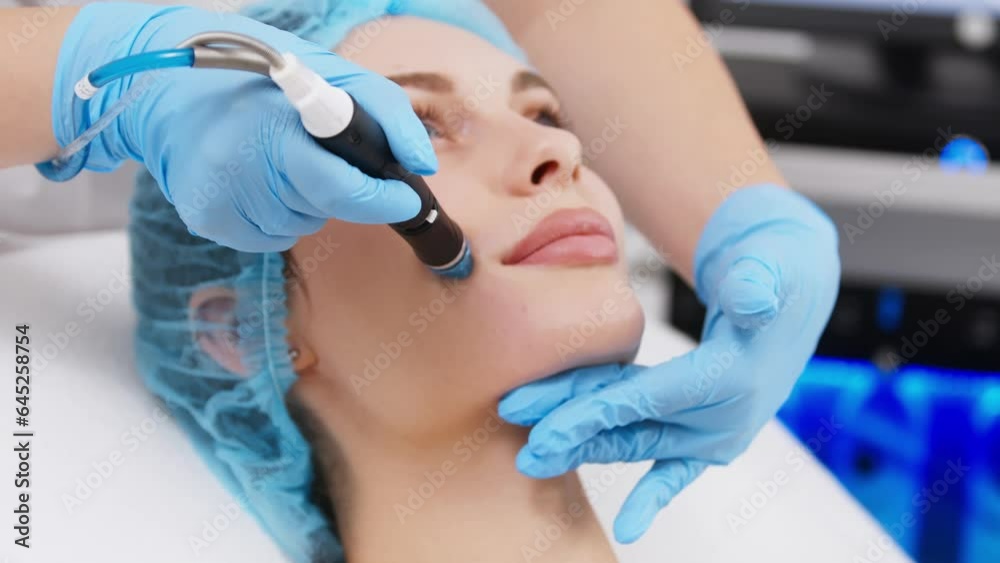 Professional dermatologist in medical gloves doing hydro peeling procedure for beautiful woman patient in cosmetology clinic. Close up facial treatment. Professional dermatologist in medical gloves doing hydro peeling procedure for beautiful woman patient in cosmetology clinic. Close up facial treatment.