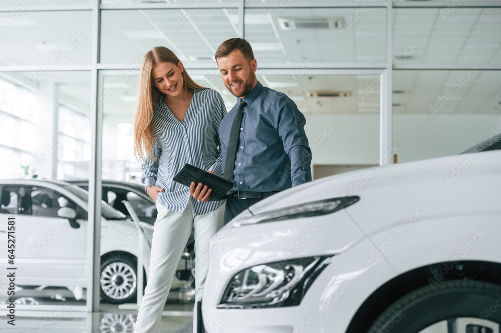Helping the customer. Man in formal clothes is with woman with the electric car Helping the customer. Man in formal clothes is with woman with the electric car