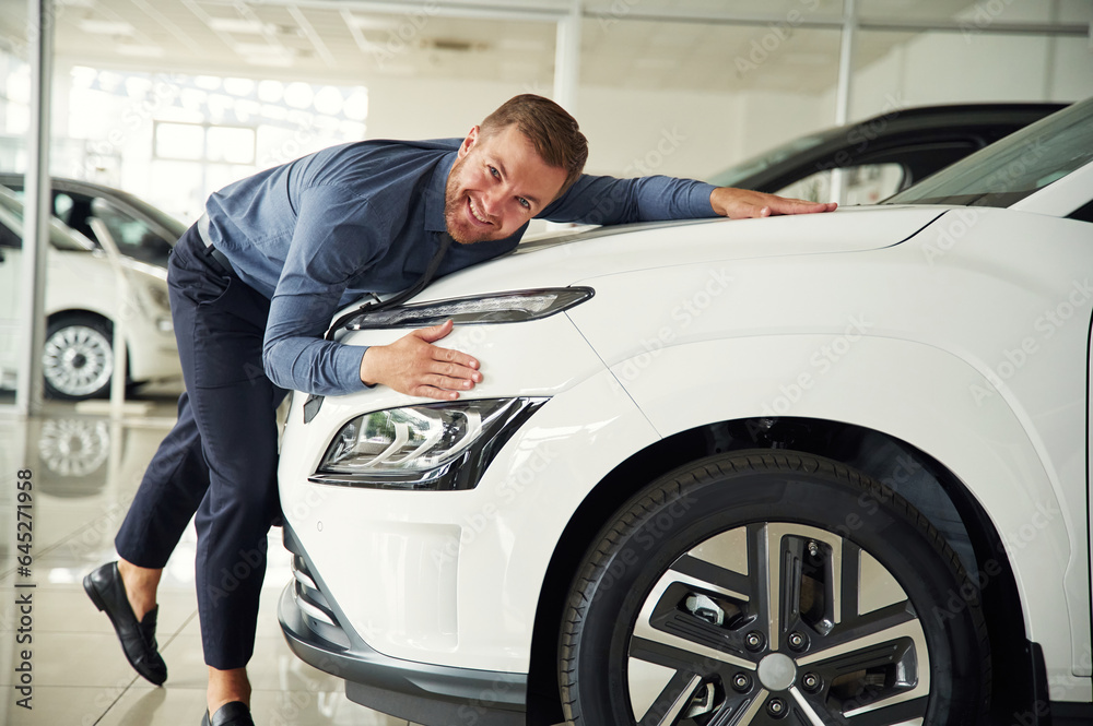 Embracing the new automobile. Handsome car dealership worker is with electric vehicle Embracing the new automobile. Handsome car dealership worker is with electric vehicle