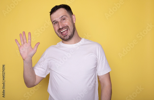 Hello Hi Young cheerful handsome bearded man greeting with open hand  enjoying communication  isolated on yellow background. Body language.