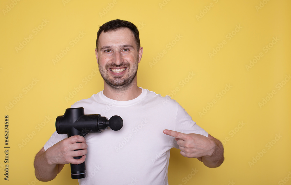 Young man wearing white clothes spend time in home gym hold and pointing on massage gun isolated on yellow background. Young man wearing white clothes spend time in home gym hold and pointing on massage gun isolated on yellow background.