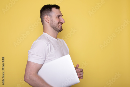 Amazed smiling handsome young bearded man holding underarm laptop pc computer isolated on yellow background. photo