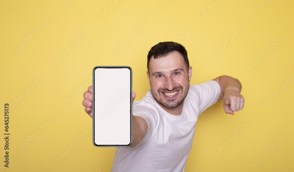 Happy excited young man showing smartphone isolated on yellow background presenting cellphone mobile offer application ads concept.