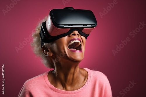 Old woman happy and smiling while wearing VR virtual reality glasses goggles headset, pink background, aged gaming