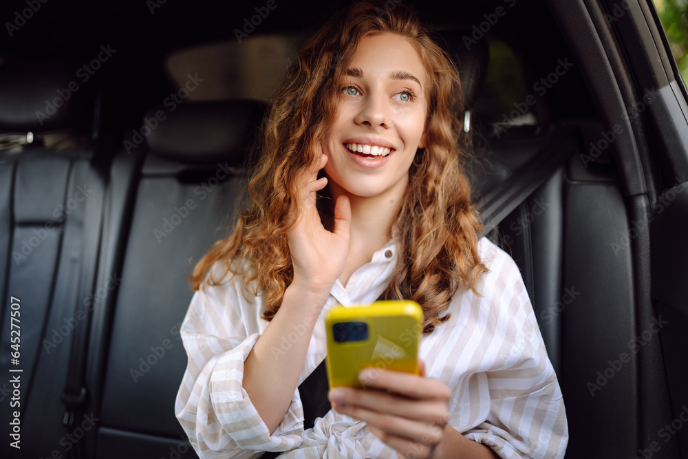 Beautiful young woman uses a smartphone while sitting in the back seat of a car. Concept of technology, traveling by car, business.