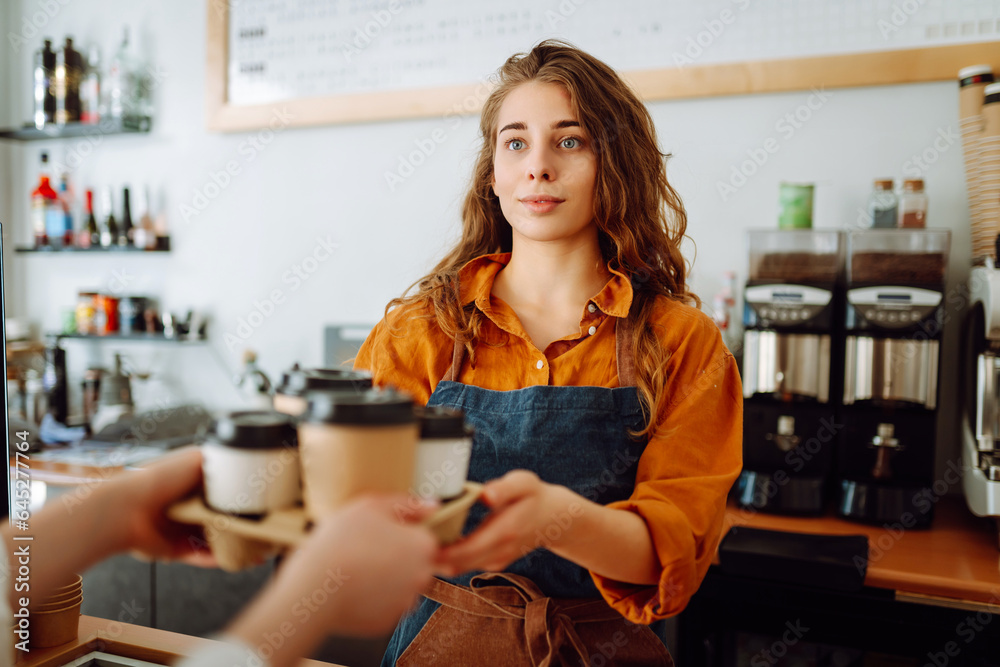 Takeaway food concept. A beautiful female barista gives to-go coffee to a client. Owner of a small business, a coffee shop,  behind the bar. Business concept.