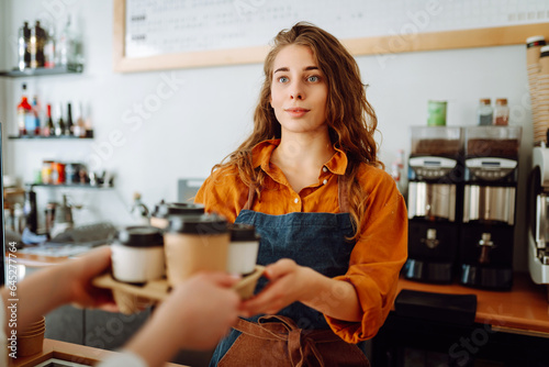 Takeaway food concept. A beautiful female barista gives to-go coffee to a client. Owner of a small business, a coffee shop, behind the bar. Business concept.