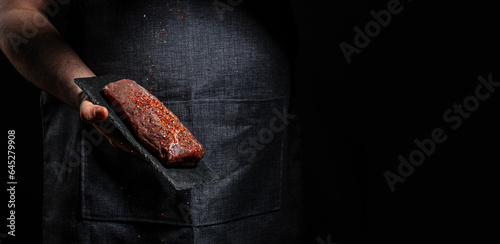 Fototapeta Naklejka Na Ścianę i Meble -  cooking meat steak and adding seasoning, beef steaks with grilled spices on dark background. Restaurant menu, dieting, cookbook recipe