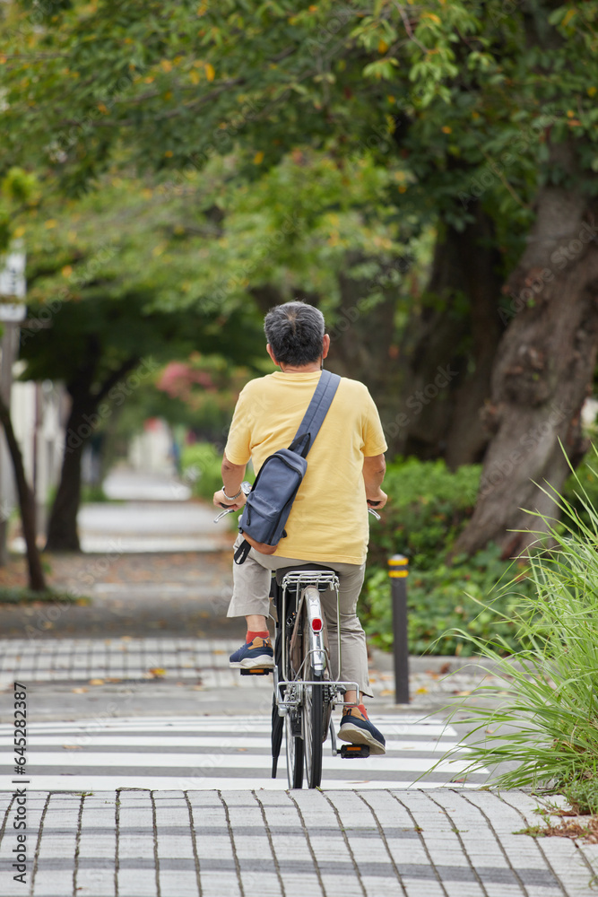 夏の昼の住宅街で自転車を乗っているシニア男性の後姿