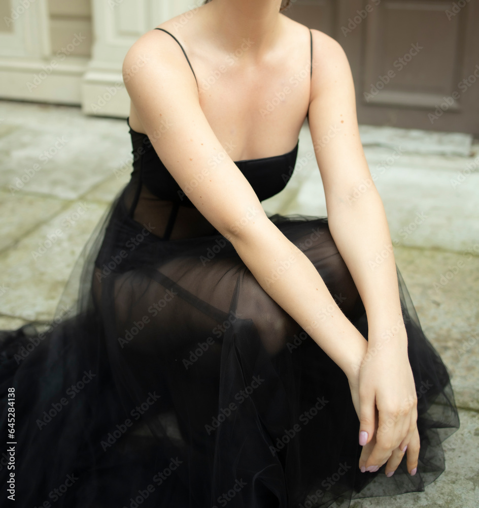 Obraz premium a 30-year-old girl sits near the house in a black, transparent, revealing dress. Style and elegance, fatal girl, photo shoot in a black dress, cheating