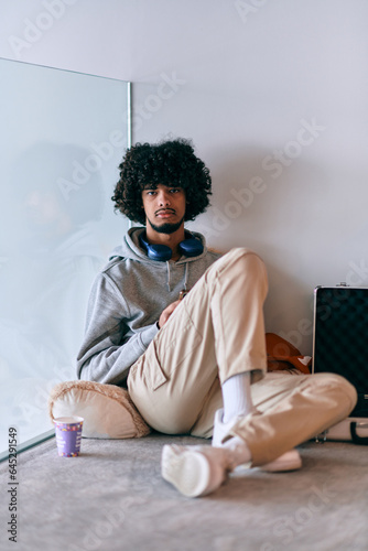  African-American entrepreneur taking a relaxing break from work, sitting on the floor while using wireless headphones and a smartphone for some digital entertainment.
