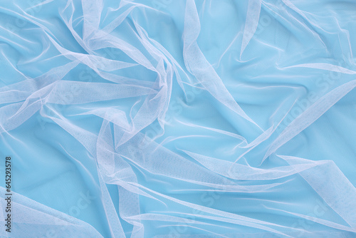 Wavy pattern of bright tulle fabric on soft colorful blue background. Abstract light chiffon, clean beautiful net cloth with wrinkle mesh lace texture loosely draped to make design patterns. .