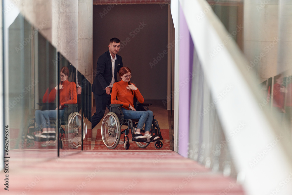 Obraz premium A company director assists his business colleague in a wheelchair, helping her navigate to their startup office, where they work alongside their diverse team of colleagues, emphasizing inclusivity and