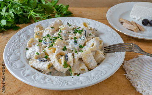 Pasta dish with ricotta cheese, tuna, black olives and parsley. On the side: a small plate with the ingredients, fresh parsley, a cotton napkin and a fork.