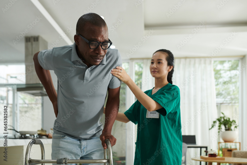Fototapeta premium Patient crying from acute pain in lower back when trying to make steps with walker for the fist time