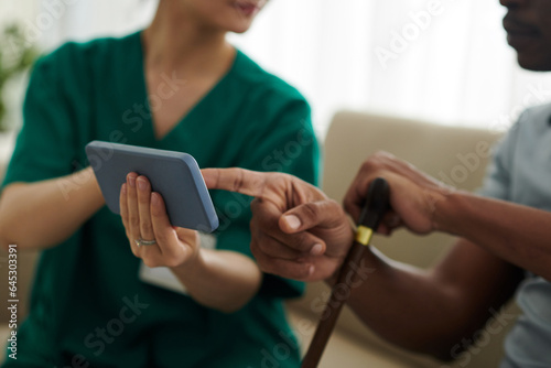 Medical nurse visiting patient at home and showing him telemedicine application on smartphone