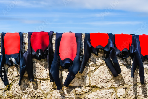 Wetsuits drying on a coastal stone wall. photo