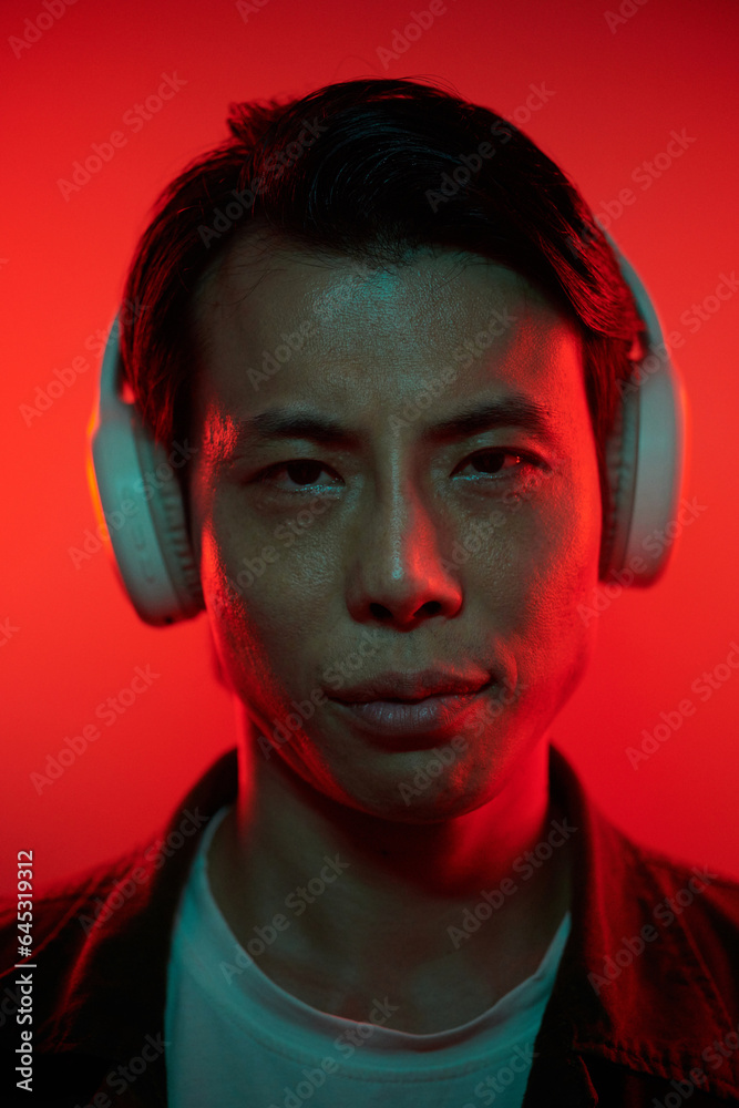 Portrait of serious Vietnamese man wearing headphones and looking at camera Portrait of serious Vietnamese man wearing headphones and looking at camera