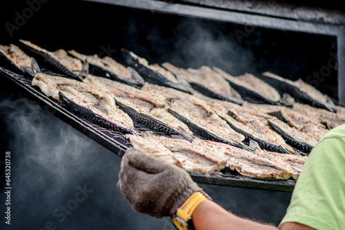 Fototapeta Naklejka Na Ścianę i Meble -  Smoking fresh mackerel fish in a mobile smokehouse in a farmer's street market in Vilnius, Lithuania