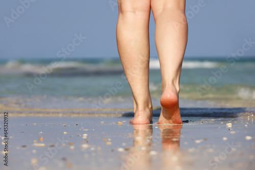 Barefoot girl walking by the sand on sea waves background. Female legs close up, beach vacation