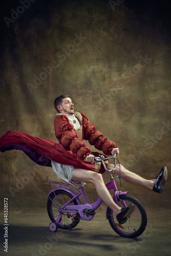 Photography Young man, medieval royal person in female dress riding little bike on vintage background