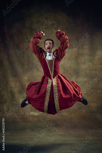 Canvas Print Young emotional man, medieval royal person emotionally jumping in female dress against vintage background