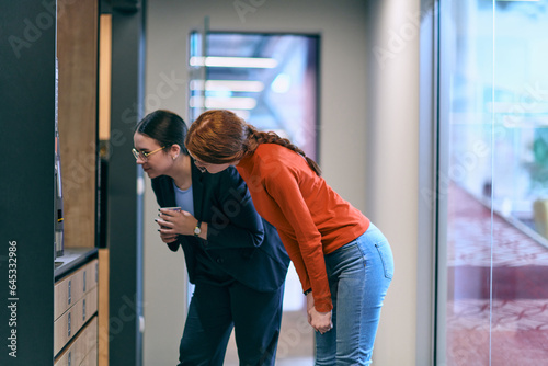 Amidst the contemporary and spacious office setting, two modern young women engage in conversation during a work break, reflecting the importance of relaxation and collaboration in the dynamic