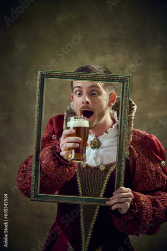 Photography Medieval royal person, prince in female dress holding picture frame and drinking beer against dark green background