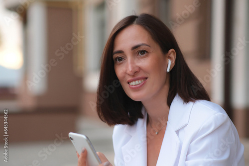Obraz na plátně A young beautiful fashionable woman is listing to music in headphones and holding a mobile phone
