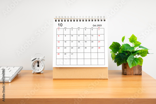 The October 2023, Monthly desk calendar for 2023 year on wooden table with alarm clock.