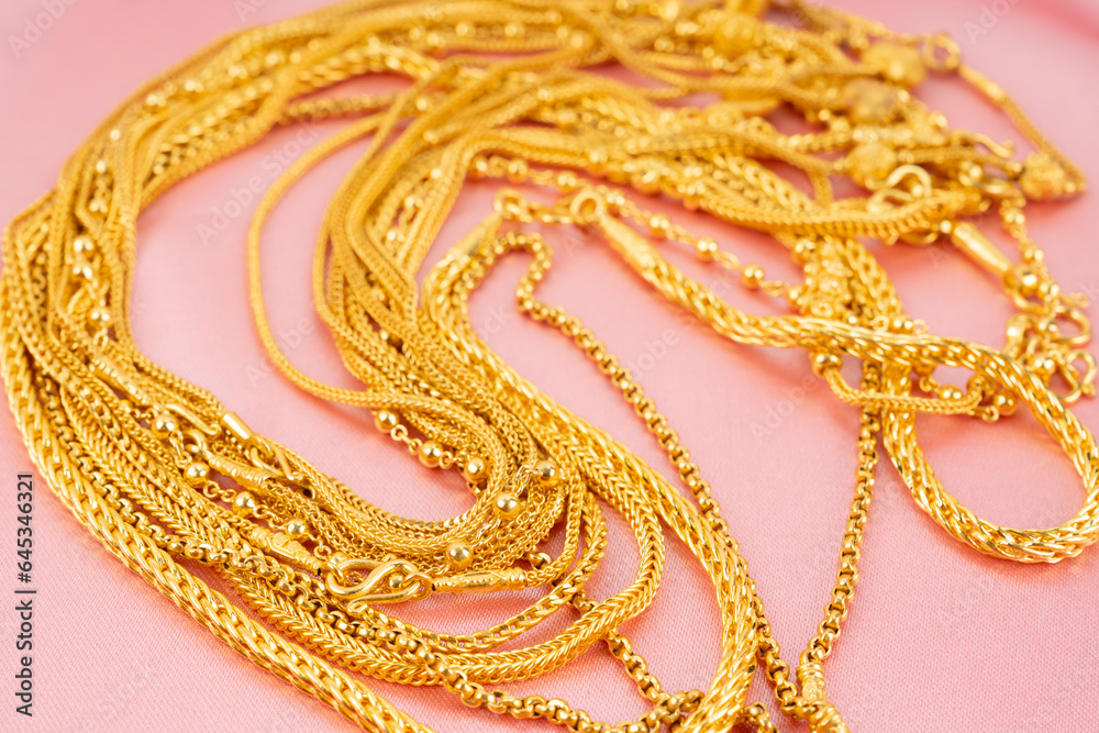 The Many gold necklaces on pink color cloth background.