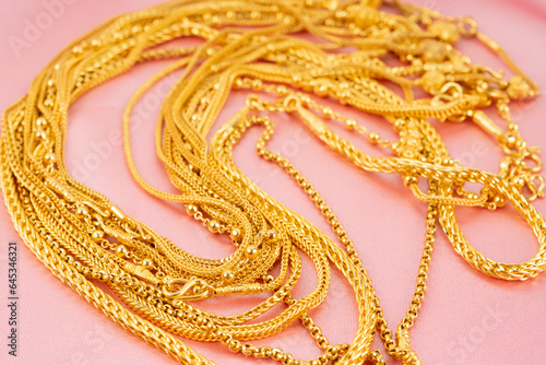 The Many gold necklaces on pink color cloth background.