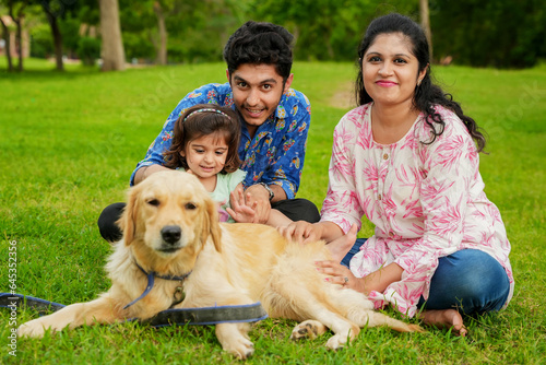 Happy young indian family having fun together at summer park. Mother, father and daughter with labrador dog in garden.
