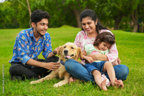 Happy young indian family having fun together at summer park. Mother, father and daughter with labrador dog in garden.
