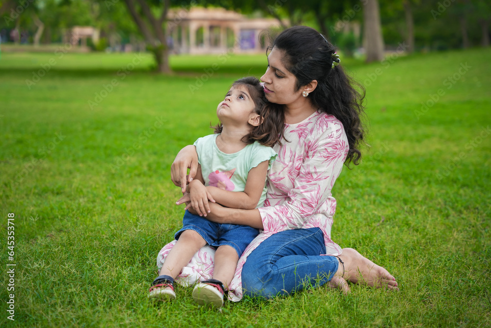 Happy young indian mother and cute little girl daughter sitting at summer park or garden. Happy young indian mother and cute little girl daughter sitting at summer park or garden.