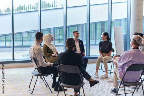 A diverse group of young business entrepreneurs gathered in a circle for a meeting, discussing corporate challenges and innovative solutions within the modern confines of a large corporation