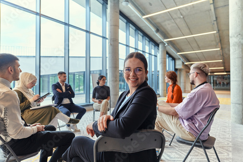 A diverse group of young business entrepreneurs gathered in a circle for a meeting, discussing corporate challenges and innovative solutions within the modern confines of a large corporation