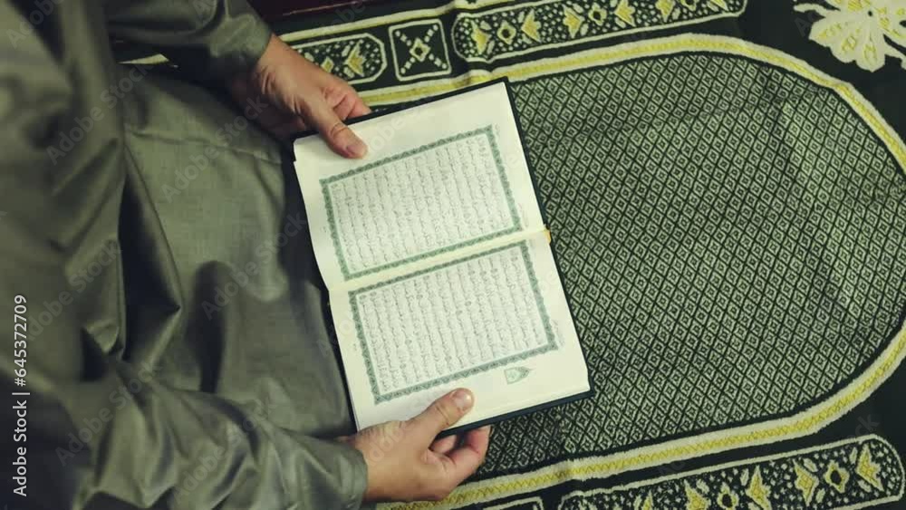 Muslim man reading The Quran holy book on a prayer mat