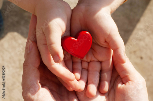 Child holds a heart in his palms. Children's hands in the hands of their parents. Protection of children and childhood. Child care. Children with heart disease.