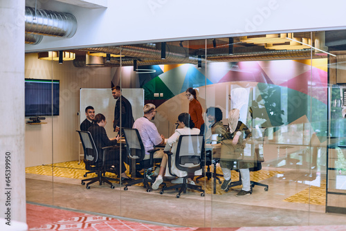 In the vibrant ambiance of a modern startup office, a diverse group of businesspeople gathers around a meeting table, exemplifying teamwork, collaboration, and the dynamic spirit of contemporary photo