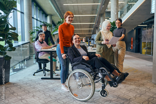A diverse group of business colleagues is having fun with their wheelchair-using colleague, demonstrating their attention and inclusivity in the workplace
